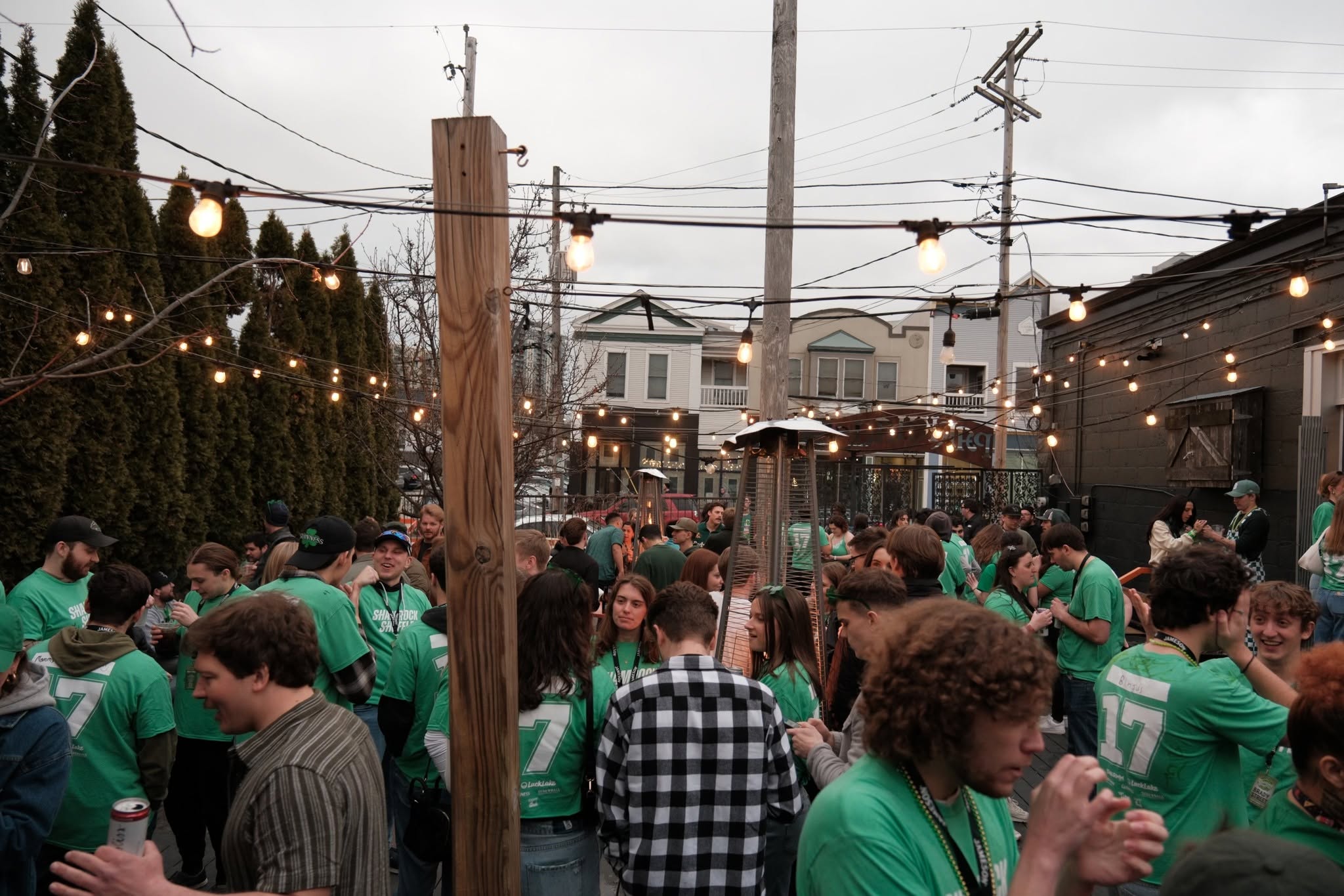 A packed back patio under strings of bulbs, the whole crowd in green shirts